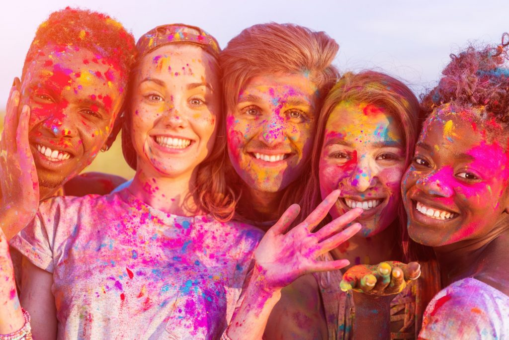 happy young multiethnic friends having fun with colorful powder at holi festival and looking at